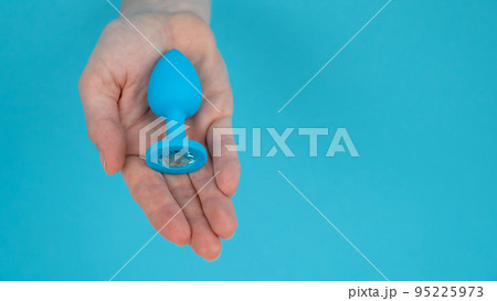 Woman holding a blue anal plug on a blue background.  Woman holding a blue anal plug on a blue background.  95225973