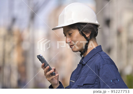 建設現場の前でスマホを見る作業服の男性 95227753