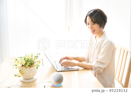 PC作業をしながらAIスピーカーに話しかける若い女性 95229132