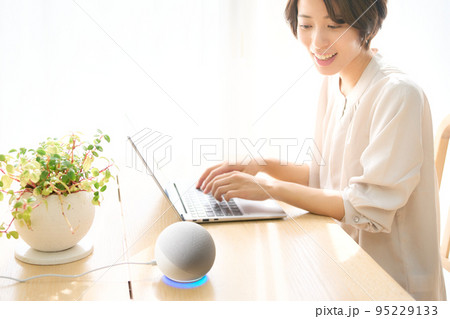 PC作業をしながらAIスピーカーに話しかける若い女性 PC作業をしながらAIスピーカーに話しかける若い女性 95229133