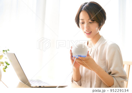 AIスピーカーを手に取って話しかける若い女性 95229134