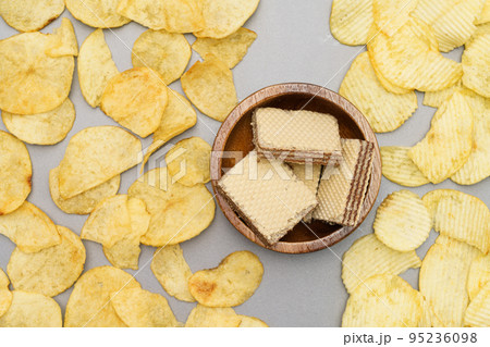 Flat lay of snack, Wafers in wooden bowl placed in center of crispy potato chips on gray background 95236098