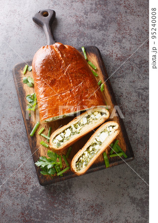 Delicious savory pie stuffed with boiled eggs, green onions, parsley, dill and spinach close-up on a wooden board. Vertical top view Delicious savory pie stuffed with boiled eggs, green onions, parsley, dill and spinach close-up on a wooden board. Vertical top view 95240008