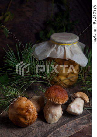 Three porcini mushrooms commonly known as Boletus Edulis and glass jar with canned mushrooms on vintage wooden background.. 95240886