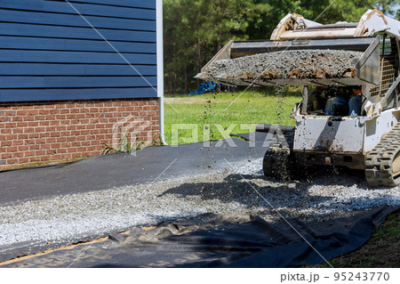 Tractor has uploaded gravel preparation platform on which storage shed will be installed near house Tractor has uploaded gravel preparation platform on which storage shed will be installed near house 95243770