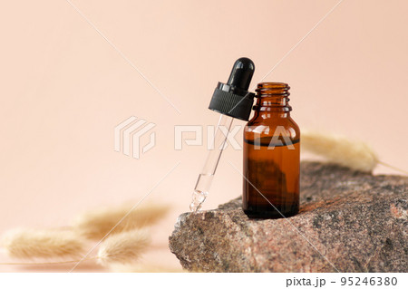 Oil, serum, fruit peeling. Cosmetic amber glass dropper bottle on wooden podium with pampas grass in soft focus. Natural beauty product presentation, pastel background. Web banner, mockup 95246380