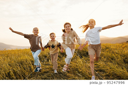 Group of happy joyful school kids boys and girls running with holding hands in field on sunny day 95247996