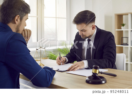 Professional lawyer or attorney signing some documents during a meeting with his client Professional lawyer or attorney signing some documents during a meeting with his client 95248011