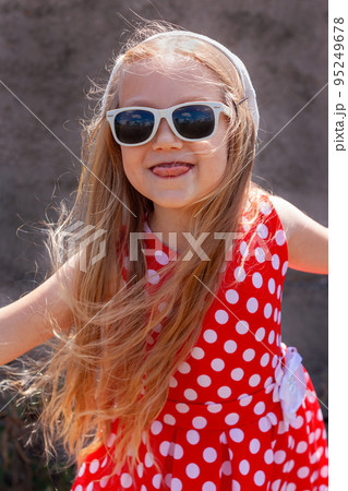 Beautiful happy girl in a red polka dot dress smiling on on concrete wall background. Cute joyful child with long hair. Beautiful happy girl in a red polka dot dress smiling on on concrete wall background. Cute joyful child with long hair. 95249678