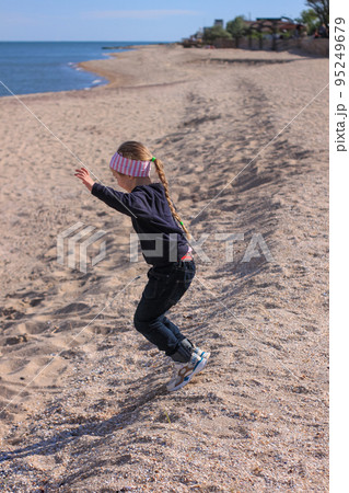 Beautiful little blond hair girl with long braid in blue hoody on sea landscape background. The child staying back view 95249679