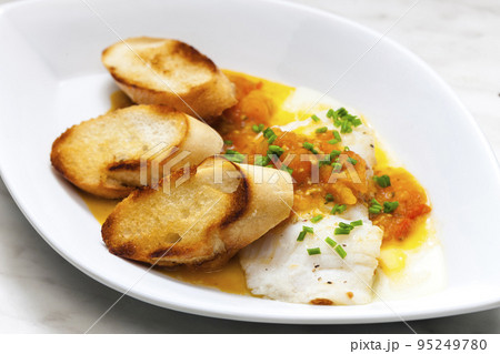 white fish with tomato sauce and roasted baguette slices 95249780