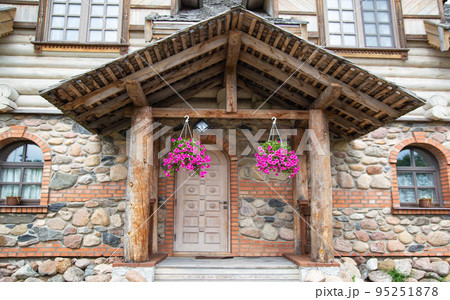 Wooden porch with massive shutters and hanging flowerpots under the roof in a stone building 95251878