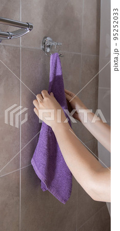 A girl hangs a lilac towel on a wall hanger in the bathroom to dry it, close-up A girl hangs a lilac towel on a wall hanger in the bathroom to dry it, close-up 95252033