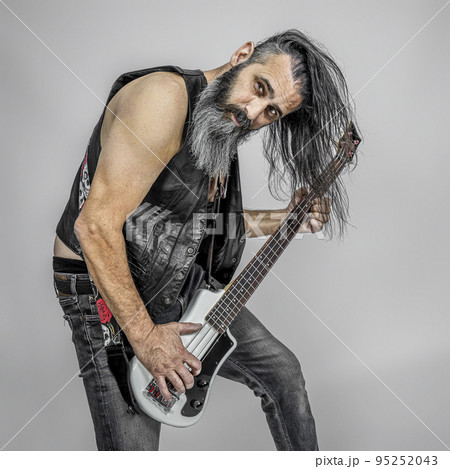 man with long hair playing the electric bass guitar. 95252043
