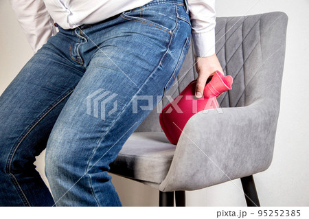A male office worker with a red breast in his hands sits on a chair. The concept of back pain in office workers. Intervertebral hernia, pain in the coccyx. Close-up A male office worker with a red breast in his hands sits on a chair. The concept of back pain in office workers. Intervertebral hernia, pain in the coccyx. Close-up 95252385