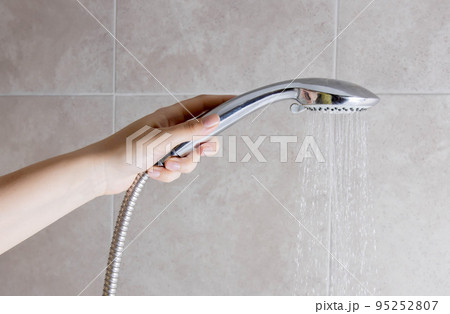 A woman holds a shower head in her hand against the background of a wall in the bathroom. Copy space for text 95252807