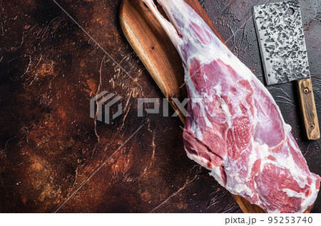 Raw whole lamb leg thigh on butcher board. Dark background. Top view. Copy space 95253740