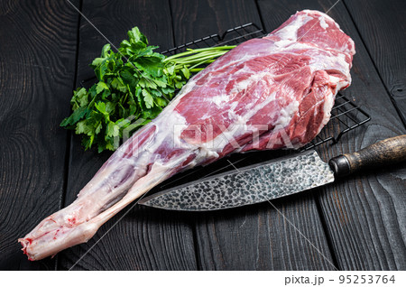 Fresh Raw whole lamb mutton leg thigh on kitchen table with herbs. Black Wooden background. Top view 95253764