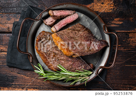 Grilled picanha or top sirloin beef steak with rosemary in steel tray. Wooden background. Top view Grilled picanha or top sirloin beef steak with rosemary in steel tray. Wooden background. Top view 95253876
