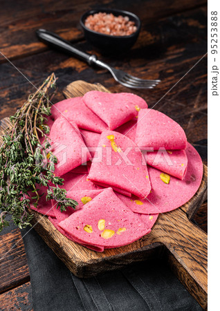 Round pieces of meat sausage with pistachios on wooden board with herbs. Wooden background. Top view Round pieces of meat sausage with pistachios on wooden board with herbs. Wooden background. Top view 95253888