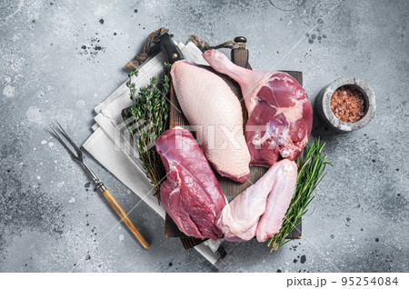 Butchered whole duck, raw breast steak, legs, wings on a butcher cutting board. Gray background. Top view 95254084