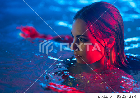 Sexy dangerous woman in swimming pool water under neon colorful light. Party in club, attractive Sexy dangerous woman in swimming pool water under neon colorful light. Party in club, attractive 95254234