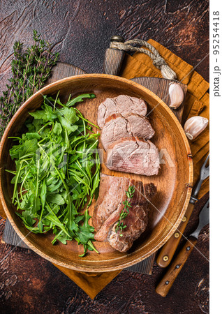 Juicy tenderloin Steak, sliced Roast beef in wooden plate with arugula. Dark background. Top view Juicy tenderloin Steak, sliced Roast beef in wooden plate with arugula. Dark background. Top view 95254418