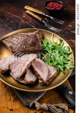Roast Tri Tip or sirloin bottom beef steak on a plate with arugula. Dark background. Top view 95254495