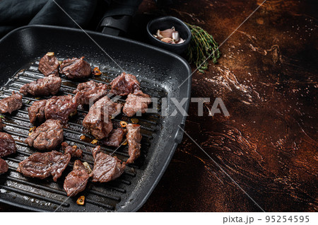 Diced beef cubes roasting in a grill pan for stew or goulash. Dark background. Top view. Copy space 95254595