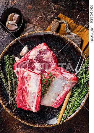 Uncooked Raw veal Short Ribs on rustic plate with rosemary. Dark background. Top view 95254936