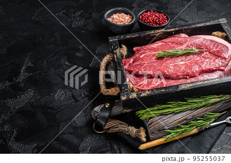 Marbled beef steak, raw meat with spices in wooden tray. Black background. Top view. Copy space Marbled beef steak, raw meat with spices in wooden tray. Black background. Top view. Copy space 95255037