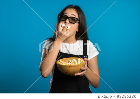 Young asian girl in 3d glasses watching fascinating comedy movie, laughing and eating popcorn on Young asian girl in 3d glasses watching fascinating comedy movie, laughing and eating popcorn on 95255220