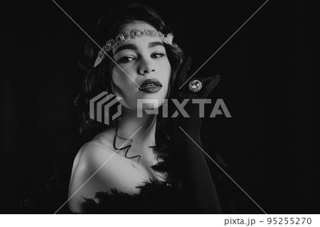 Black and white portrait of lady dressed in roaring twenties era with feathers boa on dark 95255270