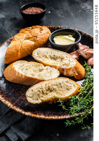 Garlic Spread on Toasted Baguette with Salt, Pepper, Thyme and Olive Oil in plate. Black background. Top view Garlic Spread on Toasted Baguette with Salt, Pepper, Thyme and Olive Oil in plate. Black background. Top view 95255648