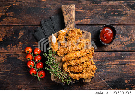 Crispy fried Breaded chicken strips, breast fillet meat with tomato ketchup on a plate. Wooden backgrund. Top view Crispy fried Breaded chicken strips, breast fillet meat with tomato ketchup on a plate. Wooden backgrund. Top view 95255952