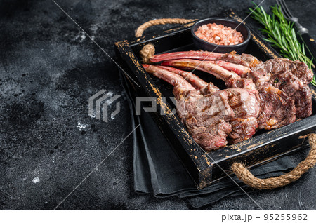 Grilled lamb chop steak, mutton meat cutlet in wooden tray. Black background. Top view. Copy space Grilled lamb chop steak, mutton meat cutlet in wooden tray. Black background. Top view. Copy space 95255962