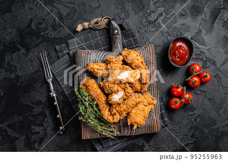 Dip fried Breaded chicken breast strips with tomato ketchup on a wooden board. Black backgrund. Top view Dip fried Breaded chicken breast strips with tomato ketchup on a wooden board. Black backgrund. Top view 95255963