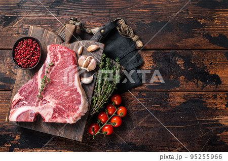 Prime T-bone beef meat steak, raw porterhouse steak on butcher board with herbs. Wooden background. Top view. Copy space 95255966