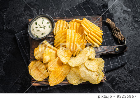 Delicious Potato chips - Crinkle, homemade, hot BBQ on a wooden board. Black background. Top view Delicious Potato chips - Crinkle, homemade, hot BBQ on a wooden board. Black background. Top view 95255967
