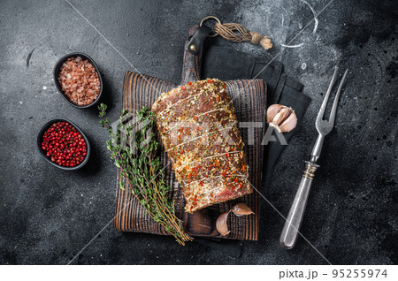 Uncooked spicy pork meat roulade prepared to roast with herbs and spices. Black background. Top view 95255974