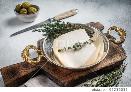 French hard goat cheese in a skillet with herbs. White background. Top view French hard goat cheese in a skillet with herbs. White background. Top view 95256055