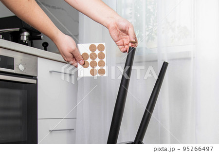 A man glues protective pads on the legs of a chair. Protection against floor scratches and noise A man glues protective pads on the legs of a chair. Protection against floor scratches and noise 95266497