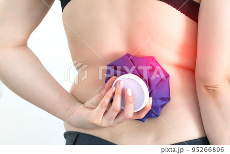 Girl holding a medical ice bag on the back of the spine. Concept for pain relief from muscle spasms and bruising pain. Therapeutics Girl holding a medical ice bag on the back of the spine. Concept for pain relief from muscle spasms and bruising pain. Therapeutics 95266896