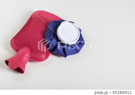 Red medical water heater and blue ice bag on a white background. The concept of treating diseases with heat and cold, heat therapy. Copy space for text Red medical water heater and blue ice bag on a white background. The concept of treating diseases with heat and cold, heat therapy. Copy space for text 95266911