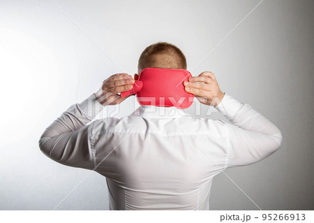 A man holds a heating pad with hot water on the back of his head. Muscle relaxation and vasodilatation of the head, thermotherapy. Headache treatment, close-up 95266913