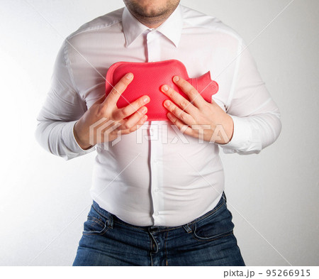 A man in a white shirt holds a red heating pad with hot water on his chest. Treatment of inflammation of the lungs and bronchitis by heating. Thermotherapy, close-up 95266915