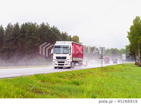 Semi-trailer truck driving on the highway with other cars during heavy rain in summer, wet road. Traffic on the road, keeping the distance, background. Sanctions 95266919