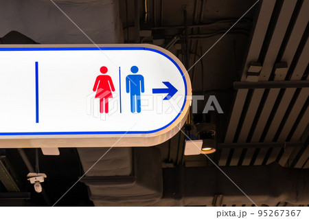 Toilet sign with a red woman and a blue man symbol and an arrow pointing the way. 95267367