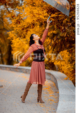 Beautiful girl in a dress with an umbrella in the autumn park. She holds him over her head, autumn leaves are falling out of him 95268828