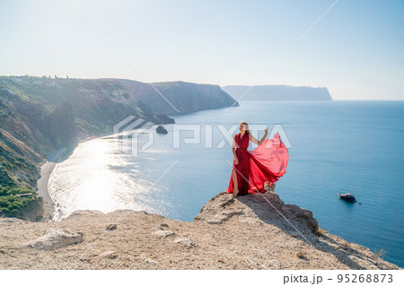 A woman in a red flying dress fluttering in the wind, against the backdrop of the sea. 95268873